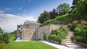 Una casa moderna con fachada de piedra, exterior blanco y una escalera de piedra que sube a un balcón.