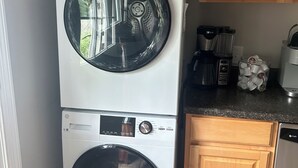 Una lavadora y secadora apiladas en una cocina con gabinetes de madera y una cafetera sobre la encimera.