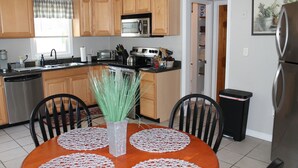 Una cocina con armarios de madera, un refrigerador de acero inoxidable, un microondas y un lavamanos. Hay una mesa de comedor con un florero de plantas verdes.