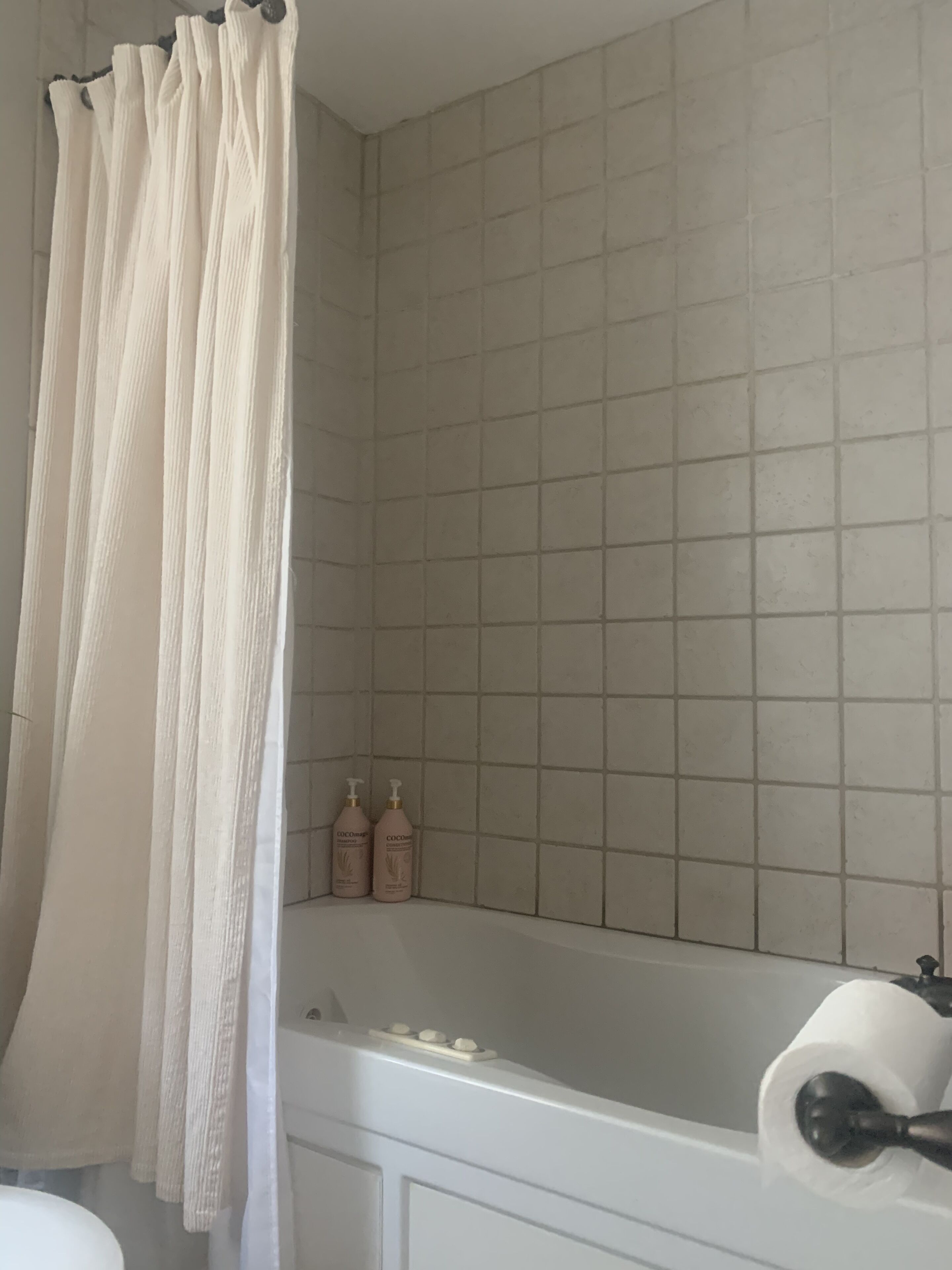 Ett badrum med badkar, duschdraperi och två flaskor schampo.