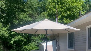 Un patio al aire libre con una mesa, sillas, un paraguas grande y una parrilla.
