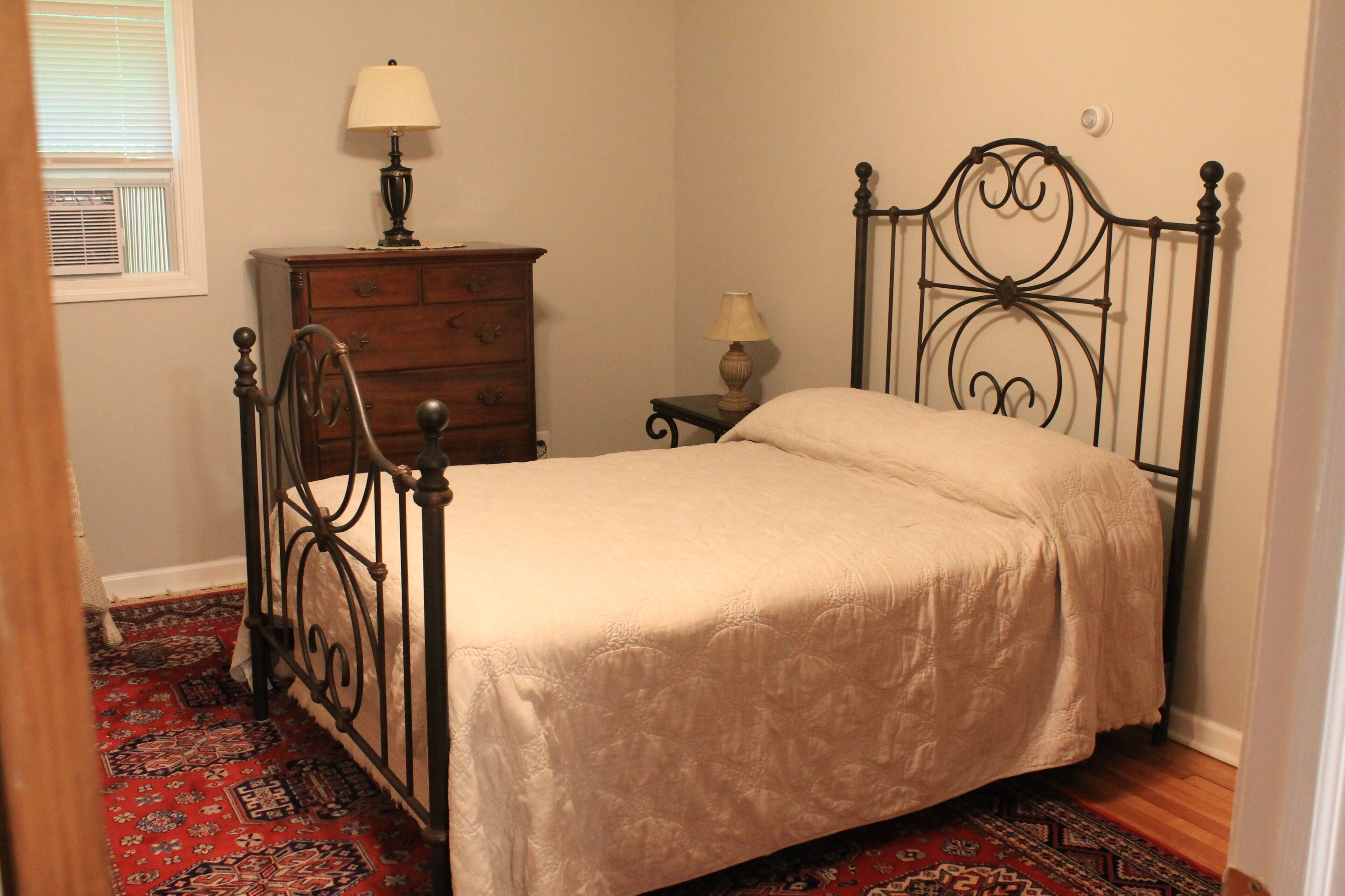 A bedroom with a bed, a dresser, a nightstand, and a lamp.