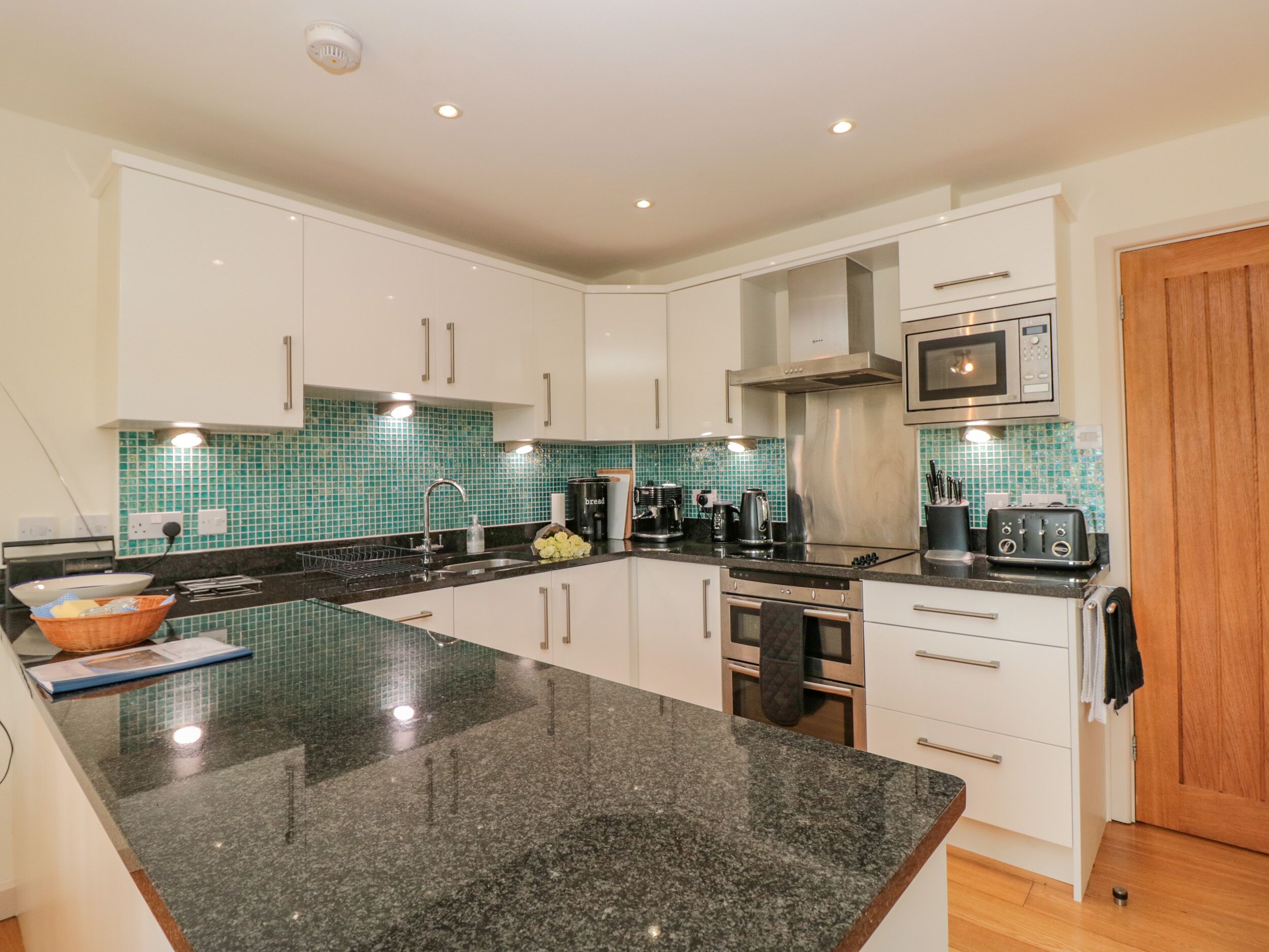 A modern kitchen with white cabinets, a granite countertop, a stainless steel range hood, a microwave, and a toaster.