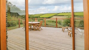 A wooden deck with a table and chairs, overlooking a green landscape with fields and a cloudy sky. - Kestrel, 19 Dartmouth Green (Totnes)