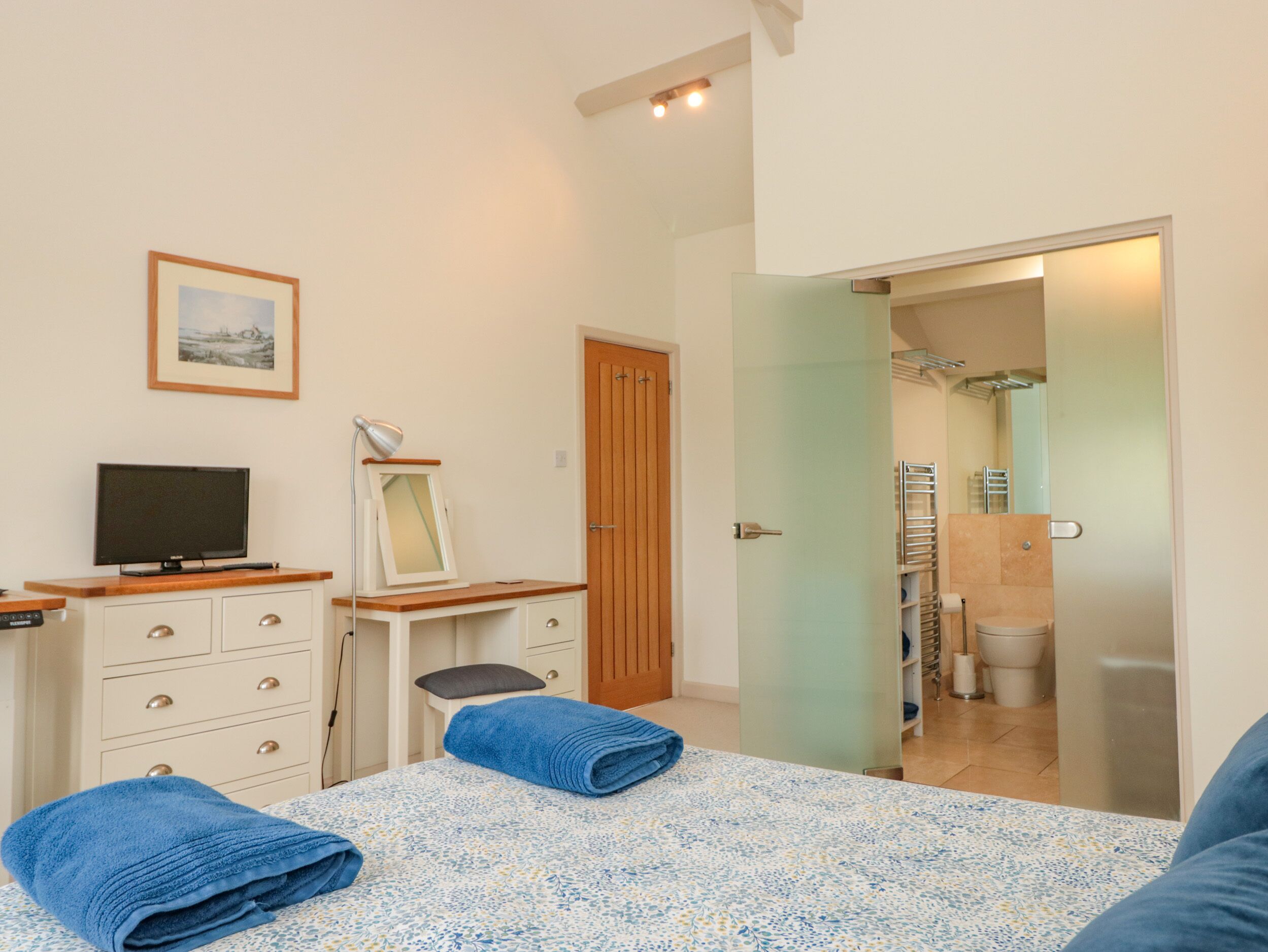 A bedroom with a bed, a desk, a television, a mirror, and a door leading to a bathroom.