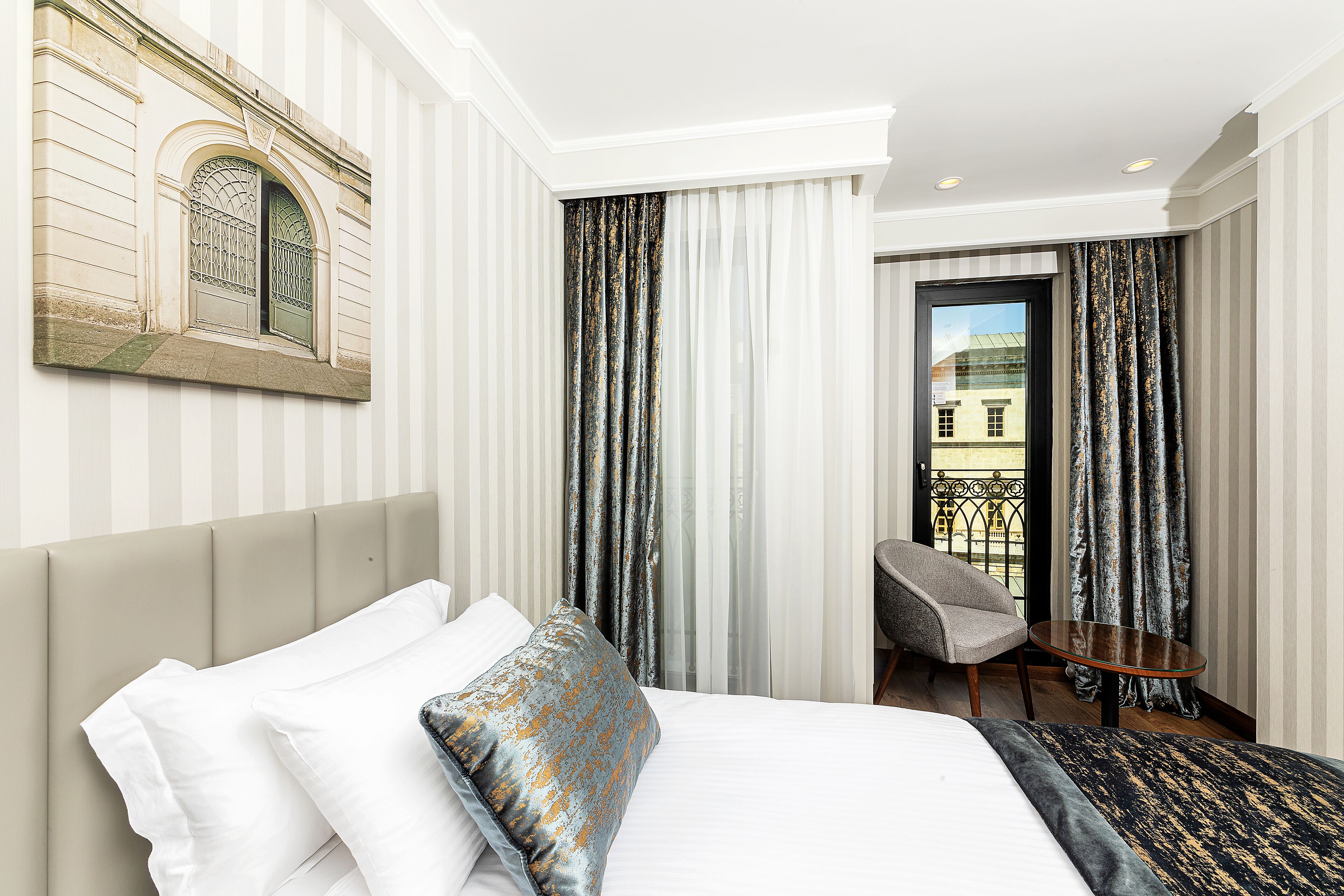 A hotel room with a bed, a chair, a small table, and a view of the outside.