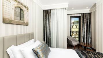 A hotel room with a bed, a chair, a small table, and a view of the outside.