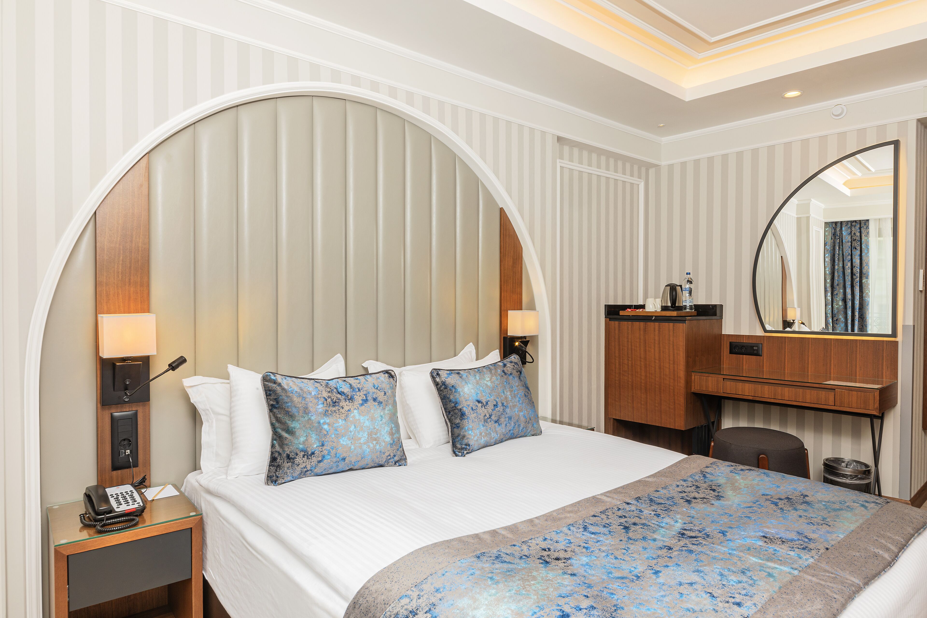 A hotel room with a large bed, a desk, a mirror, and a telephone on the nightstand.