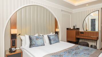 A hotel room with a large bed, a desk, a mirror, and a telephone on the nightstand.