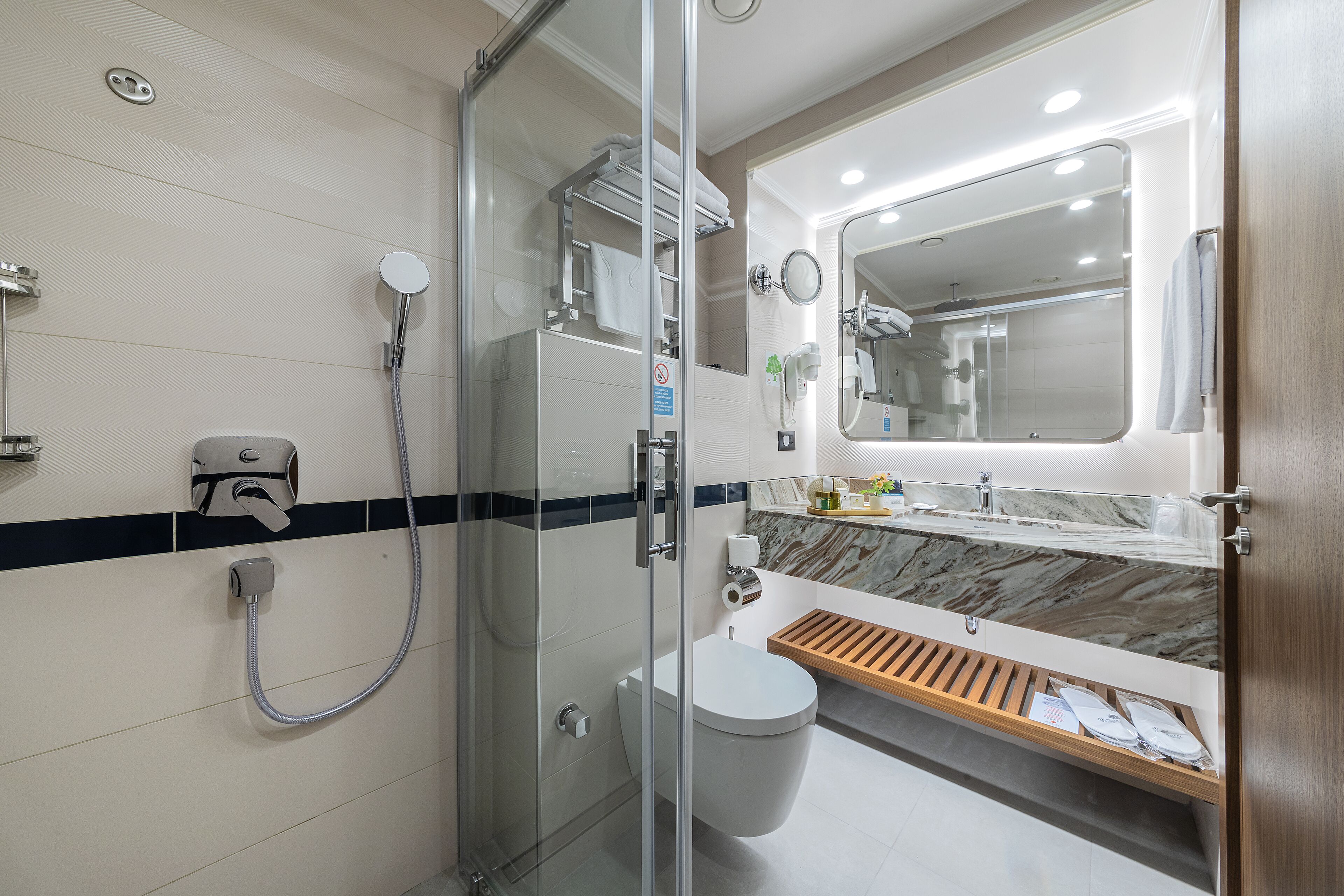 A modern bathroom with a glass-enclosed shower, a toilet, and a sink with a marble countertop.