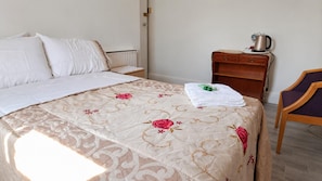 A hotel room with a bed, a nightstand, a chair, and a radiator.