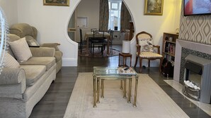 A living room with a sofa, a glass coffee table, a fireplace, and a dining area visible through an archway. - Renovated 4-bed Home, Sleeps 9 With Parking & Spa (Blackpool)