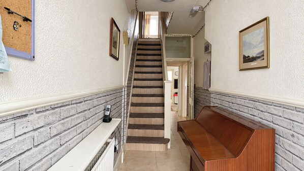 Un pasillo con una escalera, un banco, un tablón de corcho con notas y un cuadro en la pared.