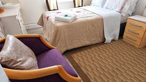 Una habitación de hotel con una cama, una mesita de noche, una silla y un pequeño aparador de madera.