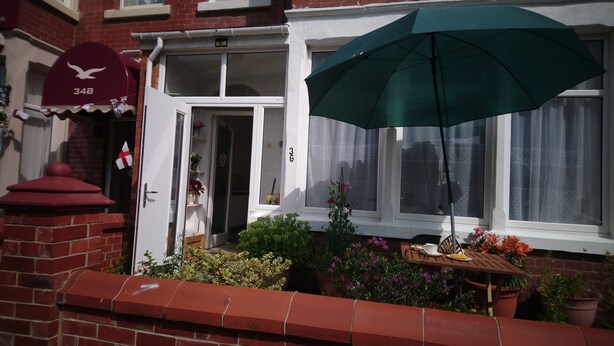 A residential house with a red brick facade, a white door, and a green umbrella. - Renovated 4-bed Home, Sleeps 9 With Parking & Spa (Blackpool)