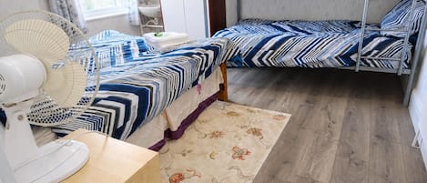 A room with two beds, a fan, a sink, and a window with curtains.