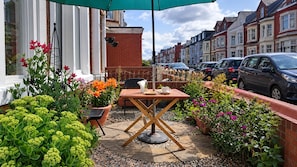 Un patio con una mesa y sillas, rodeado de plantas y flores en macetas.