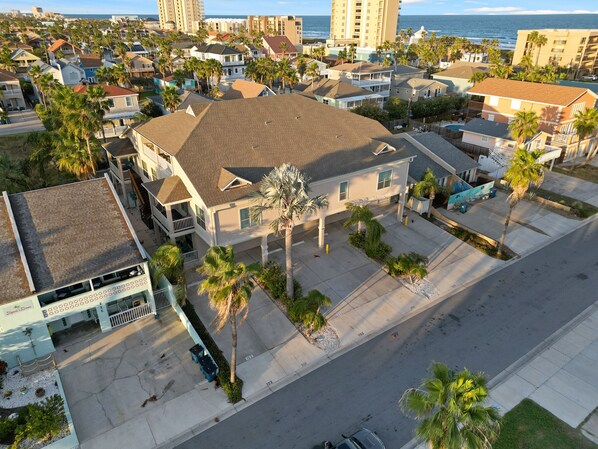 Vista aérea de una zona residencial con casas, palmeras y una playa al fondo.