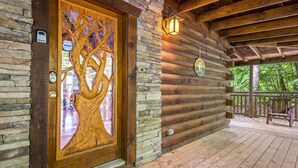 A wooden cabin with a stone wall, a wooden door with a tree design, and a porch with a bench.
