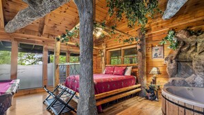 A log cabin room with a bed, a hot tub, and a large tree trunk in the center.