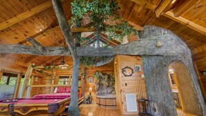 A log cabin with a wooden interior, a pool table, a red sofa, and a hot tub.