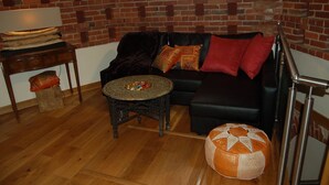 A living room with a brick wall, a black sofa with patterned cushions, a round coffee table, a small wooden side table, and a decorative orange cushion. - The Hyde Dovecote Kinver, pet Friendly Holiday let (Stourbridge)