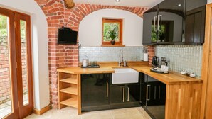 A kitchen with a brick arch, wooden countertops, a black refrigerator, and a window with a plant. - The Hyde Dovecote Kinver, pet Friendly Holiday let (Stourbridge)