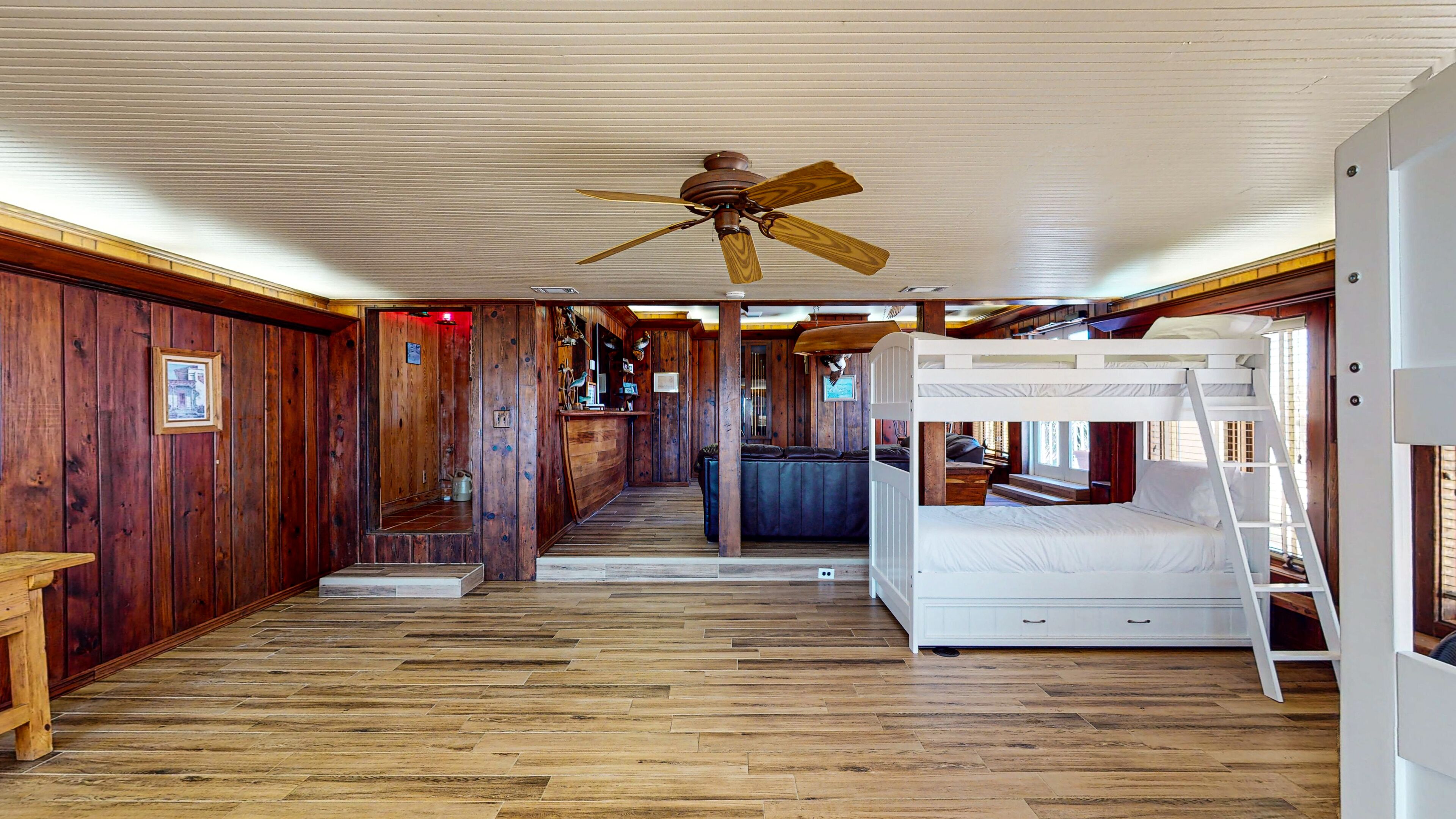 Een cabin interieur met houten vloer, stapelbedden, een plafondventilator en een houten bar.