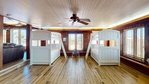 Ein Zimmer mit Holzboden, zwei Etagenbetten, einem Deckenventilator und großen Fenstern.