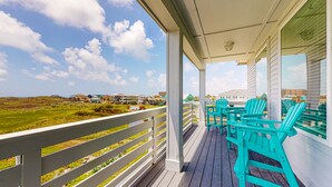 A covered porch with turquoise Adirondack chairs, a view of the beach, and a white railing.