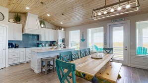 A modern kitchen with white cabinets, a large island, and a view of the beach through the windows.