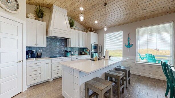 A spacious kitchen with white cabinetry, a large island, and a view of the beach through the windows.