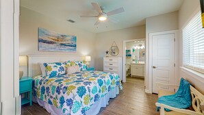 A bedroom with a bed, nightstands, a ceiling fan, a bathroom with a sink and mirror, and a chair.