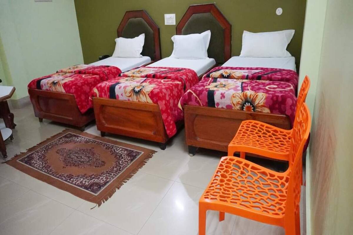 A hotel room with four single beds, a wooden chair, a small table, and a patterned rug.