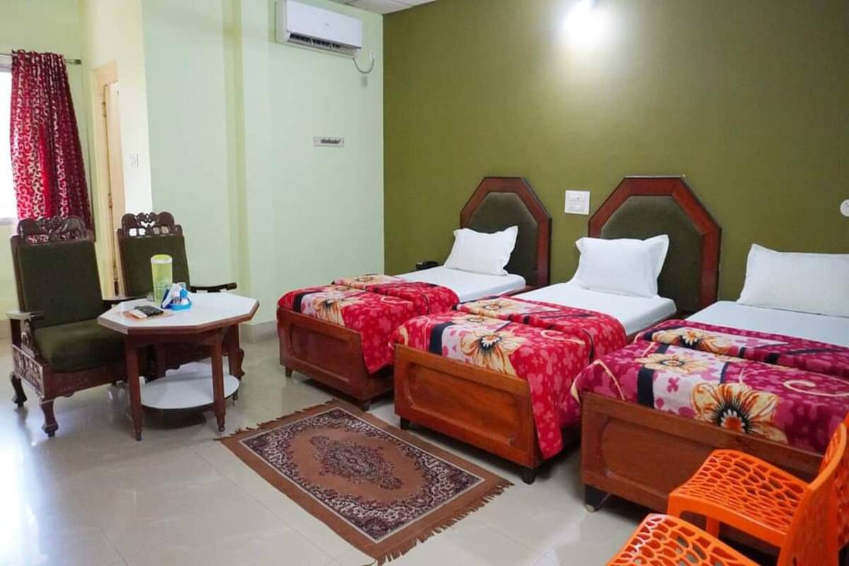 A hotel room with two beds, a chair, a small table, and a decorative rug.