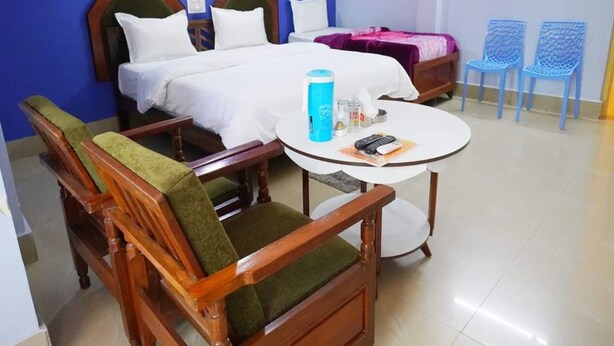 Una habitación de hotel con dos camas, una mesa redonda con una botella de agua azul y dos sillas azules.