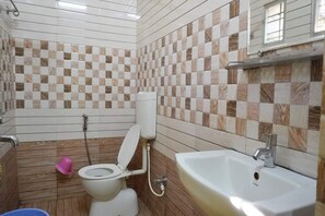 A bathroom with a tiled floor, a toilet, a sink, and a shower area.