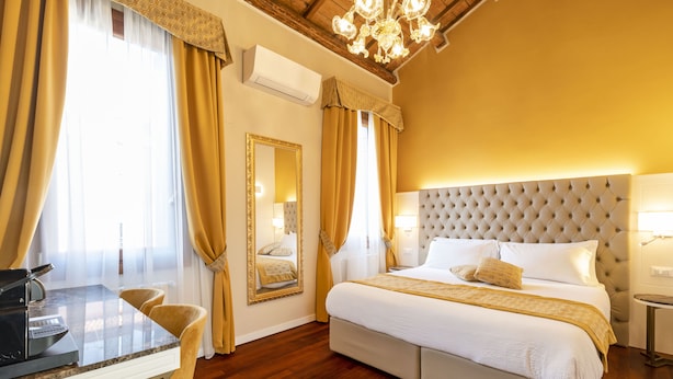 A hotel room with a large bed, a dining area with a table and chairs, a chandelier, and a large mirror.