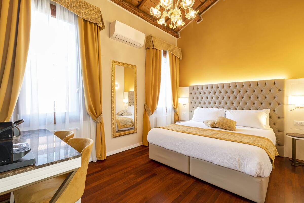 Een hotelkamer met een groot bed, een zithoek met een tafel en stoelen, een kroonluchter en een grote spiegel.