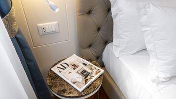 A neatly made bed with white linens, a magazine on a small round table beside it, and a wall socket.