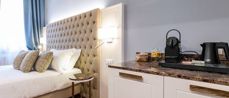 Habitació d'hotel amb un capçal de llit amb textura, una taula rodona petita, un llit amb almoinos estampats, una cafetera i una tetera a la barra.