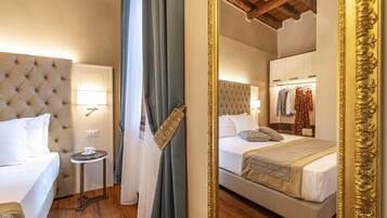 A hotel room with a tufted headboard, a bedside table with a lamp, a bed with a patterned throw, and a mirror with an ornate frame.