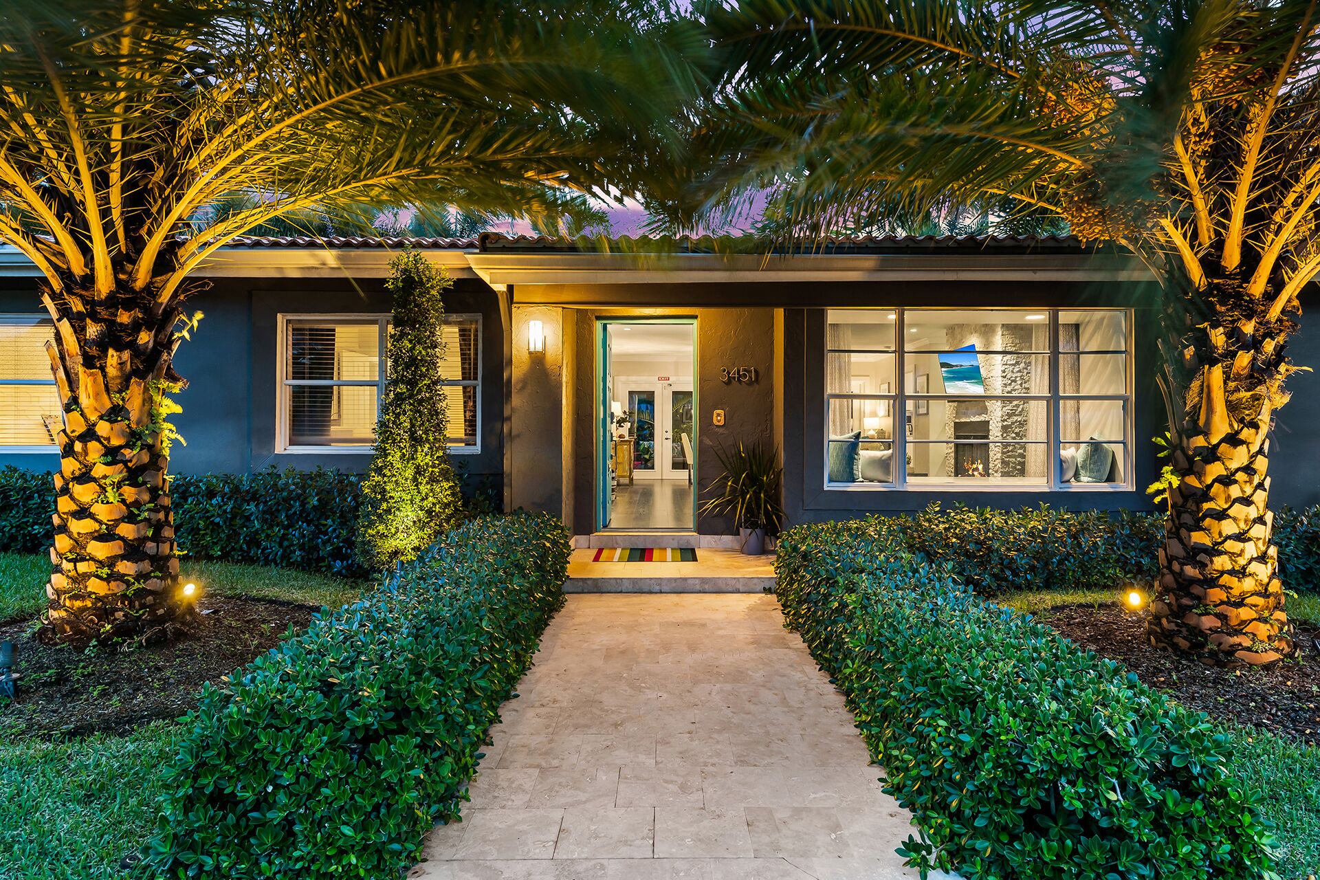 A modern house with a well-lit entrance, a stone fireplace, and a view of the interior through large windows.