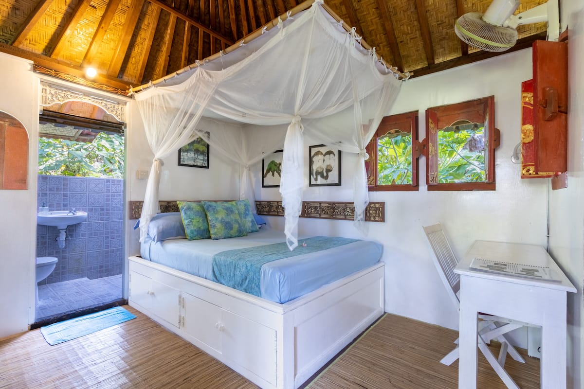 A bedroom with a canopy bed, a small desk, and a view of the outside.