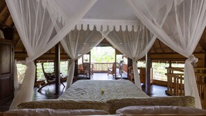 Ein Zimmer mit einem Bett, weißen Vorhängen und Blick ins Freie.