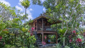 Ein zweistöckiges Holzhaus mit Balkon, umgeben von üppiger tropischer Vegetation.