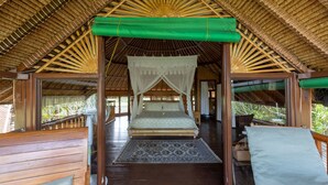 Ein Zimmer mit Holzboden, einem Bett, einem grünen Baldachin und einem gemusterten Teppich.