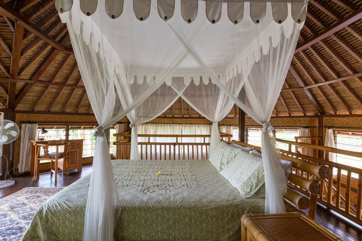 A room with a four-poster bed, wooden furniture, and a thatched roof.