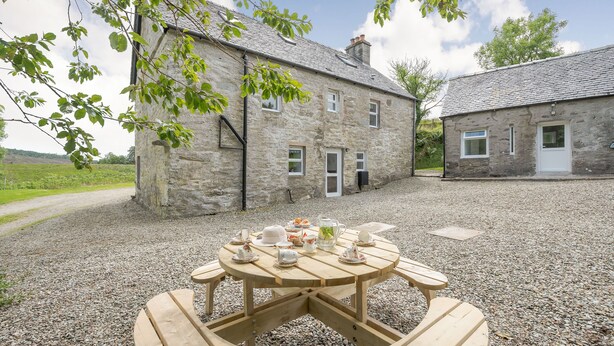 A stone building with a gravel courtyard and a wooden picnic table set up with tea cups and a teapot. - Smithy House (Lochgilphead)