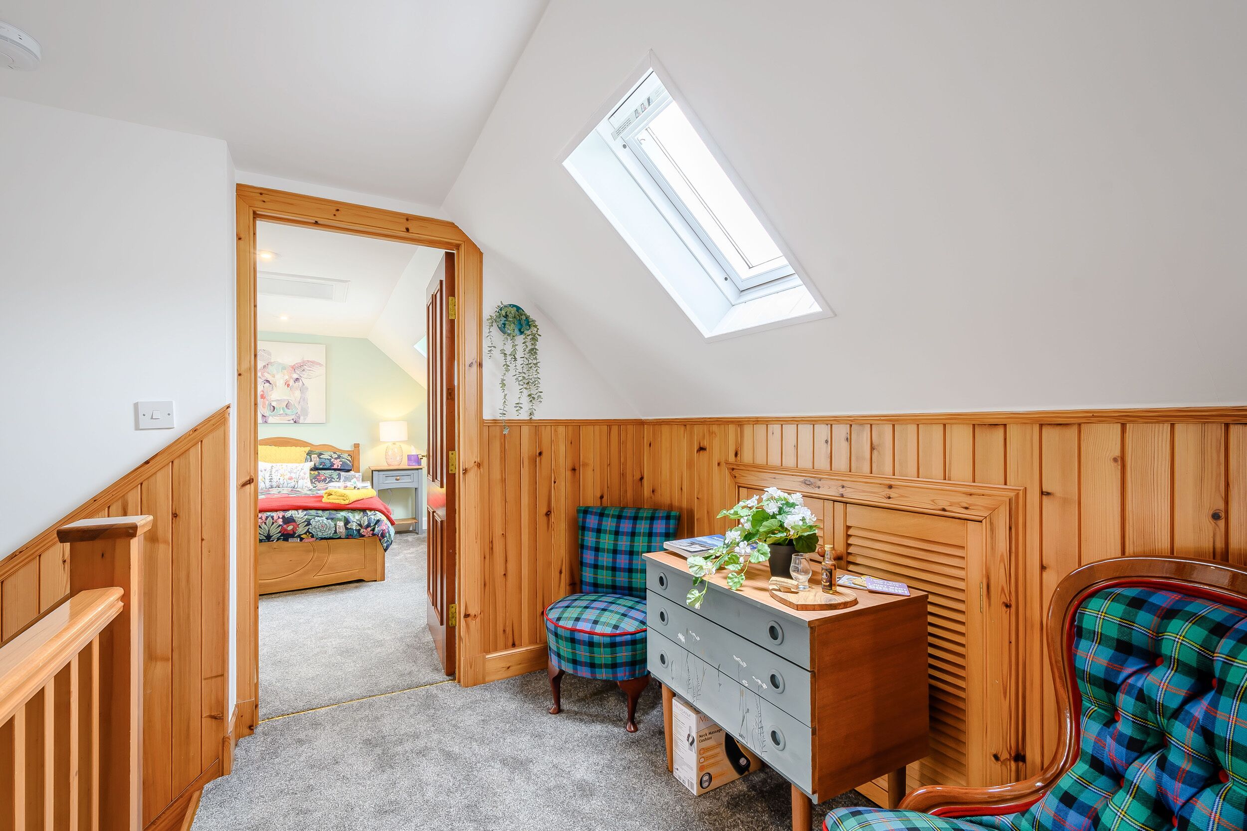 A bedroom with a skylight, wooden paneling, a dresser, a chair, and a bed in the background.